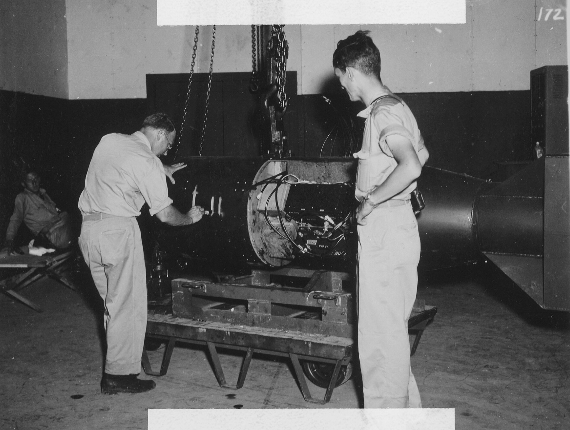 Commander A. Francis Birch assembles the Little Boy bomb while physicist Norman Ramsey watches. This is one of the rare photos where the interior of the bomb can be seen, with the fuzing units and battery boxes visible, attached around the gun tube. 